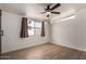 A spacious bedroom featuring wood-look floors, a ceiling fan, and a large window with neutral curtains at 3828 W Townley Ave, Phoenix, AZ 85051
