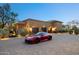Stunning exterior view of home with circular driveway and red sports car in front of the three-car garage at 10092 E Troon North Dr, Scottsdale, AZ 85262