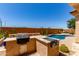 Outdoor kitchen with BBQ, pool view, desert landscaping and blue sky at 27537 W Yukon Dr, Buckeye, AZ 85396
