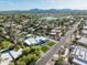 An aerial view shows the white modern home, pool, and tennis court in a desert neighborhood with mountain views at 9733 E Clinton St, Scottsdale, AZ 85260