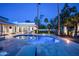 Backyard pool with travertine tile, palm trees, and lush landscaping at twilight at 9733 E Clinton St, Scottsdale, AZ 85260