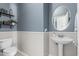 Stylish powder room with a pedestal sink, decorative mirror, shelving, and a neutral color scheme at 14318 N 142Nd Ln, Surprise, AZ 85379