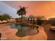 Lush backyard pool area with rock waterfall feature under a vibrant sunset sky at 15602 N 37Th St, Phoenix, AZ 85032