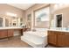 Bathroom showcasing a soaking tub with tile surround, double sinks, a large mirror and blinds on the window at 2945 E Clifton Ave, Gilbert, AZ 85295