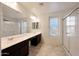 Bright bathroom featuring dual sinks, a large mirror, window and a separate glass enclosed shower at 16540 W Culver St, Goodyear, AZ 85338