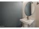 This powder room features a pedestal sink, an oval mirror, and blue accent wall at 18624 W Cathedral Rock Dr, Goodyear, AZ 85338