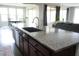 Kitchen island with dark wood cabinets, gray countertops, a stainless steel sink, and views of the living areas at 19814 W Buchanan St, Buckeye, AZ 85326