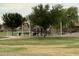 Community playground with swings, climbing area, and slide, surrounded by mature trees, adjacent to a green lawn at 36197 W Cartegna Ln, Maricopa, AZ 85138