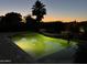 Inviting pool illuminated at dusk with lush landscaping and a silhouette of a palm tree at 16280 W Durango St, Goodyear, AZ 85338