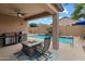 Inviting covered back patio with barbecue, ceiling fan, outdoor fireplace, and view of the refreshing pool at 41413 W James Ln, Maricopa, AZ 85138