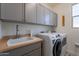Well-lit laundry room with gray cabinets, a white sink, and a modern washer and dryer at 10035 E Trent Ave, Mesa, AZ 85212