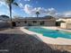 An in-ground pool is surrounded by rock landscaping in this home's backyard with solar panels at 1545 W Marco Polo Rd, Phoenix, AZ 85027