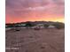 Expansive view of a large lot surrounded by a white fence under a vibrant sunset sky at 8678 S John Jacob Astor Ave, Casa Grande, AZ 85193