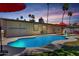 Sparkling pool surrounded by a concrete patio, lush greenery, and palm trees under a colorful sunset sky at 1535 E Kenwood St, Mesa, AZ 85203