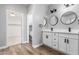 Bathroom featuring dual sinks with framed mirrors, white cabinets, and wood-look flooring at 18675 W Foothill Dr, Surprise, AZ 85387