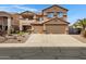 Two-story tan home featuring a three-car garage, tile roof, and low maintenance desert landscaping at 10758 E Lobo Ave, Mesa, AZ 85209