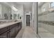 Bright bathroom features double sinks, stone countertops, and a tiled walk-in shower with glass door at 14571 W Wethersfield Rd, Surprise, AZ 85379