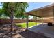 Backyard featuring a covered patio, a small section of grass, trees, and rock landscaping at 13439 W Desert Ln, Surprise, AZ 85374