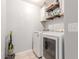 A bright laundry room featuring white appliances, floating wood shelves, and light tile flooring at 17235 W Statler St, Surprise, AZ 85388
