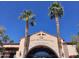 Exterior view of Corte Bella Golf Club's entrance, framed by tall palm trees against a clear blue sky at 12937 W El Sueno Ct, Sun City West, AZ 85375