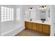 Bright bathroom with dual sinks, wood vanity, mirrored walls and a glass block window at 13620 N 82Nd Ln, Peoria, AZ 85381
