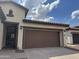 A large brown garage door featuring coach lights and a walkway to the home's entrance at 7046 N 84Th Dr, Glendale, AZ 85305