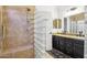 Well-lit bathroom with a tiled shower featuring a glass block wall and a double sink vanity with granite countertop at 10138 W Oregon Ave, Glendale, AZ 85307
