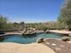 Serene backyard pool area with a rock waterfall feature, desert landscaping, and mountain views at 18359 W Sweet Acacia Dr, Goodyear, AZ 85338
