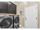 Well-lit laundry room features gray front-loading washer and dryer, complemented by dark wood cabinets at 19291 E Thornton Rd, Queen Creek, AZ 85142