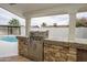 Covered outdoor kitchen area features a stainless steel grill, stone base, and poolside access at 4115 W Sierra St, Phoenix, AZ 85029