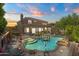 Aerial view of the well-lit backyard showcasing the pool, spa, and manicured landscaping at dusk at 10415 E Rosemary Ln, Scottsdale, AZ 85255