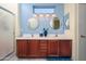 Bathroom boasts dual sinks with a vanity, decorative mirrors, modern lighting, and a glass-enclosed shower at 16527 W Blackhawk Ct, Surprise, AZ 85374