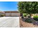 Well-manicured front yard featuring a three-car garage and lush, mature trees and shrubbery at 35654 N Vidlak Dr, San Tan Valley, AZ 85143