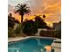 Backyard pool with clear blue water reflecting the beautiful sunset, framed by lush landscaping and palm trees at 3417 E Mission E Ln, Phoenix, AZ 85028