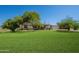 Well-maintained backyard with lush lawn, mature trees, a detached garage, and a charming ranch-style house at 3738 E Hash Knife Draw Rd, Queen Creek, AZ 85140