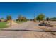 A long, dirt driveway leads to this ranch-style home with mature trees and a clear blue sky above at 3738 E Hash Knife Draw Rd, Queen Creek, AZ 85140