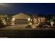 Inviting exterior of home with a two-car garage, desert landscaping, and stone accents, beautifully illuminated at night at 16077 W Vale Dr, Goodyear, AZ 85395
