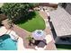 Aerial view of a serene backyard featuring a lush artificial lawn, mature shade tree, and a patio with a fire pit at 18351 W Southgate Ave, Goodyear, AZ 85338