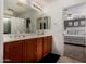 Bright bathroom with double sinks, wood cabinets, a large mirror, and a doorway to the main bedroom at 27420 N 63Rd Dr, Phoenix, AZ 85083