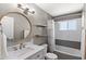 Neutral bathroom with a round mirror, granite counters, and a shower and tub combination with gray tiling and floating shelves at 3837 E Yale St, Phoenix, AZ 85008