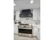 Close-up of a gourmet kitchen with a stainless steel stove, white cabinetry, and a modern black range hood at 5441 E Wethersfield Rd, Scottsdale, AZ 85254