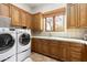 Laundry room featuring modern washer and dryer, wood cabinets, tile backsplash, and a window at 10010 E Blue Sky Dr, Scottsdale, AZ 85262