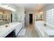 Bright and spacious primary bathroom featuring double sinks, white cabinets, wood look tile, soaking tub, and large closet at 2224 W Olive Way, Chandler, AZ 85248