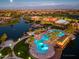 Aerial view of the community clubhouse, pool, and lake at dusk with city lights in the background at 42311 W Good Vibrations Ln, Maricopa, AZ 85138