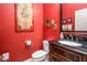 Stylish powder room featuring red walls, decorative artwork, and a dark wood vanity with a granite countertop at 42311 W Good Vibrations Ln, Maricopa, AZ 85138
