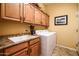 Functional laundry room with wooden cabinets, a countertop, a sink, and a modern washing machine at 42311 W Good Vibrations Ln, Maricopa, AZ 85138