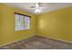 Minimalist bedroom with a neutral carpet, bright yellow walls, and ceiling fan at 13722 N 150Th Ln, Surprise, AZ 85379