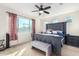 A primary bedroom with a large window, ceiling fan, and a gray upholstered bench at 18581 W College Dr, Goodyear, AZ 85395