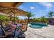 Outdoor dining space with seating for six near a pool and fireplace, shaded by an umbrella at 42293 W Good Vibrations Ln, Maricopa, AZ 85138