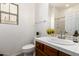 Bathroom with wooden cabinetry, tiled countertop, mirror, window, and toilet at 15674 W Mackenzie Dr, Goodyear, AZ 85395